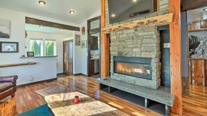 A modern living room with a stone fireplace, wooden beams, and a large window. - Bellingham Vacation Rental w/ Private Deck (Bellingham)