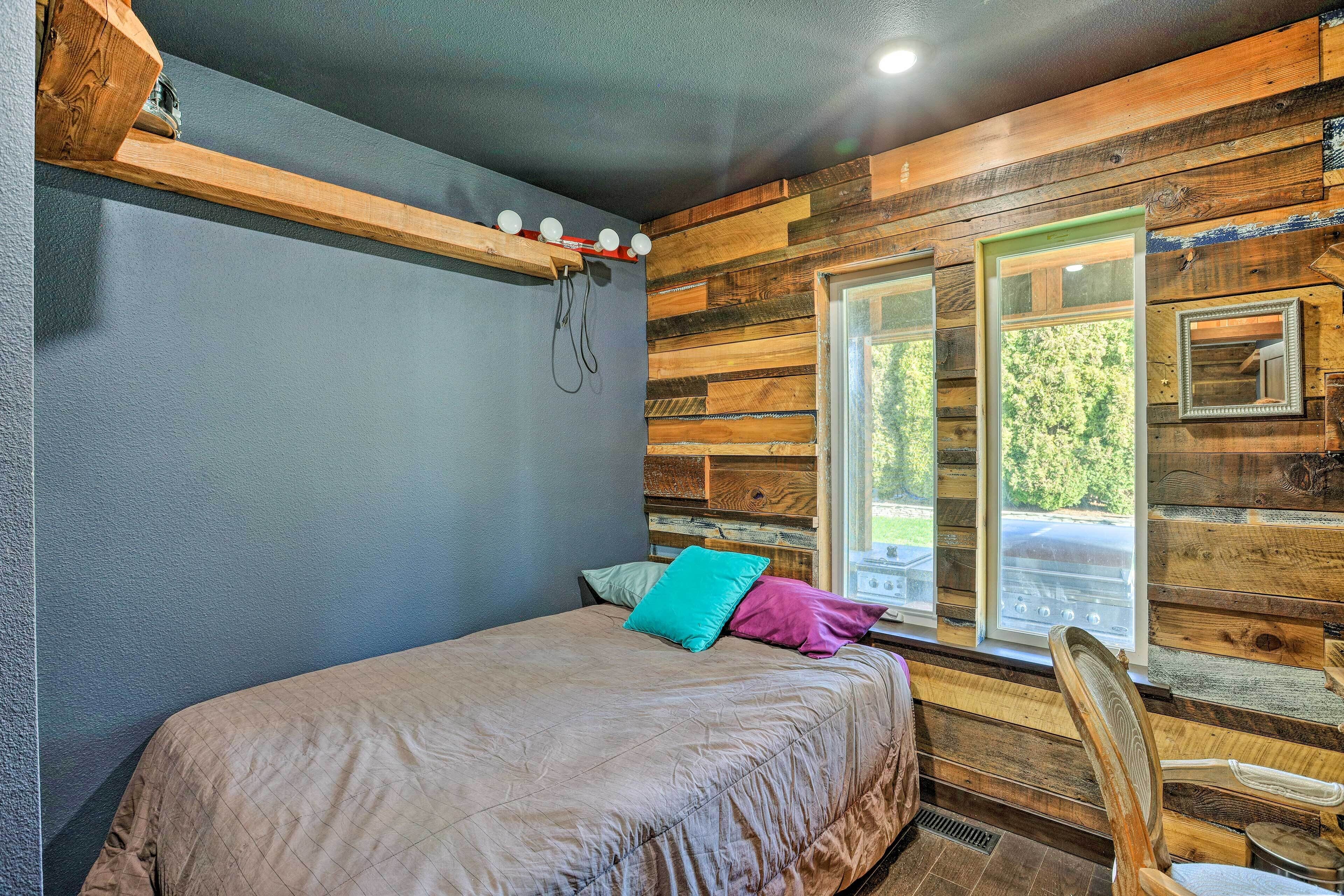 Un dormitorio con una cama, almohadas, una silla, un ventanal y paredes de madera.