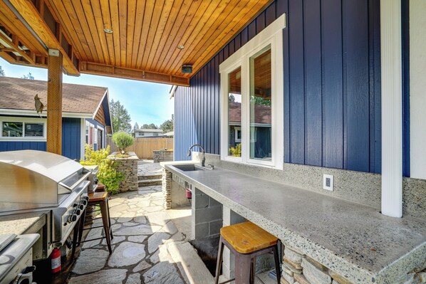 Un espace cuisine extérieur comprenant un barbecue, des tabourets de bar et une terrasse pavée de pierres.