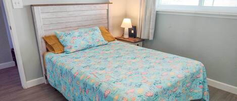 A bedroom with a bed, a nightstand, a lamp, and a window with curtains.