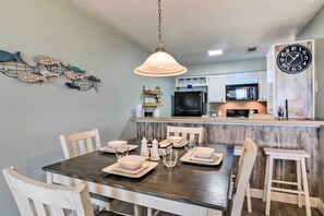 Un coin repas avec une table en bois foncé, dressée pour quatre personnes, des chaises blanches et un luminaire suspendu.