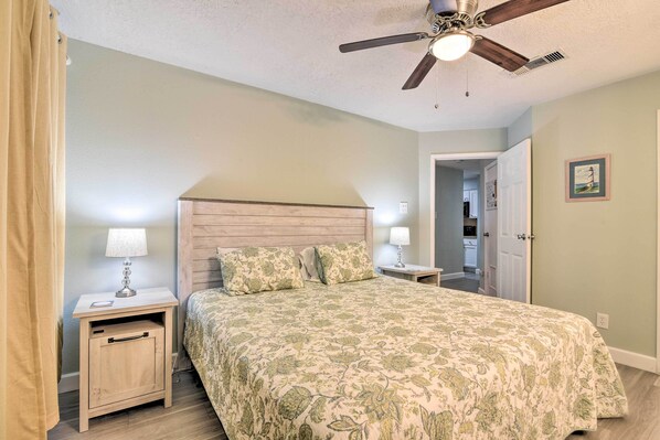 A bedroom with a bed, nightstands, a ceiling fan, and a door leading to a bathroom. - Gulf Views & Patio: Lovely Galveston Condo! (Galveston)