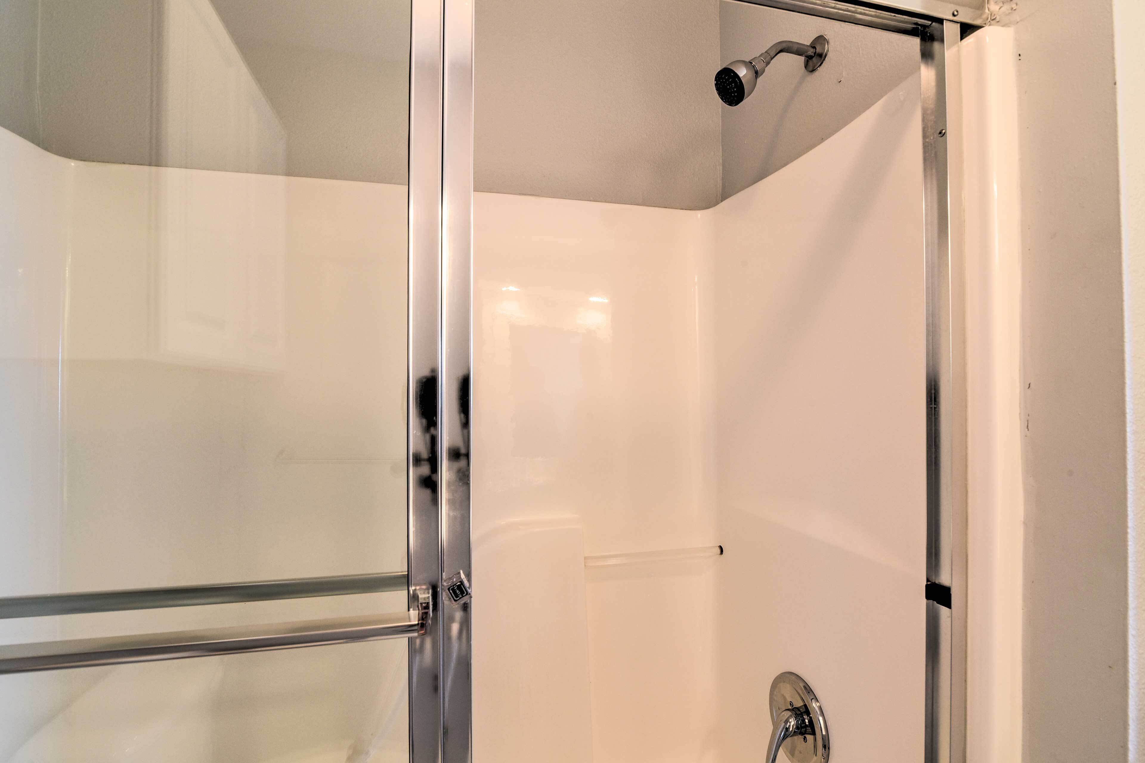 A glass-enclosed shower with a handheld showerhead and a wall-mounted faucet.