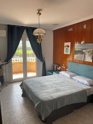 A bedroom with a bed, a nightstand, a lamp, a picture frame, and a view of the outdoors.