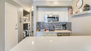 A compact kitchen with white cabinets, a microwave, a coffee maker, and a clock on the wall.