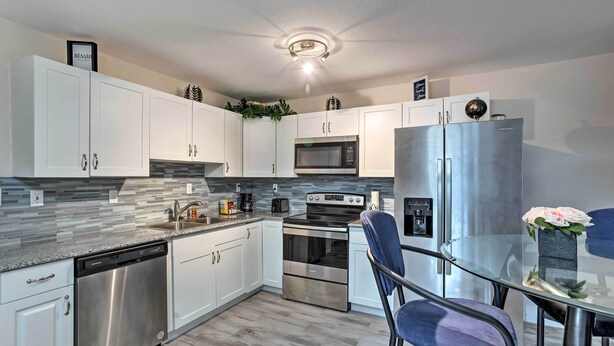 A modern kitchen with white cabinets, stainless steel appliances, a glass dining table, and a ceiling light fixture. - Ideally Located West Palm Beach Apartment! (West Palm Beach)