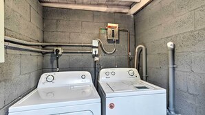 A laundry room with two white front-loading washers and dryers, grey pipes, and a control panel on the wall. - Ideally Located West Palm Beach Apartment! (West Palm Beach)