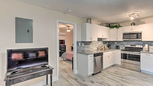 A modern kitchen with white cabinets, stainless steel appliances, and a flat-screen TV on a dark wooden stand. - Ideally Located West Palm Beach Apartment! (West Palm Beach)