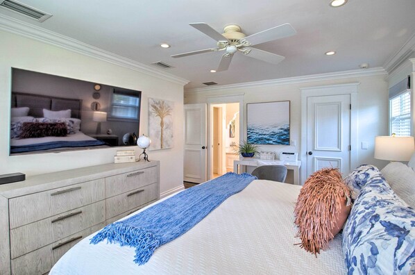 Un dormitorio con cama, televisor, escritorio y puerta que da a otra habitación.