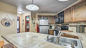 A kitchen with a large island, stainless steel sink, wooden cabinets, a microwave, and a refrigerator.