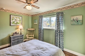 Une chambre à coucher avec un lit, une commode, une chaise et une fenêtre avec des rideaux.