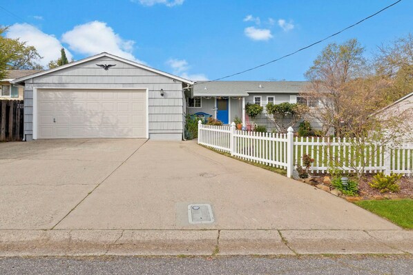Une allée menant à une maison et à un garage, avec une clôture en bois peinte en blanc.