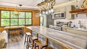 A kitchen with a large island, wooden cabinets, and a view of the outdoors. - Remodeled Cabin w/ Fire Pit on Norfork Lake! (Elizabeth)