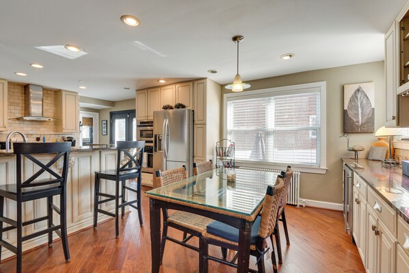 A modern kitchen with a glass-top dining table, wooden chairs, and built-in cabinetry.