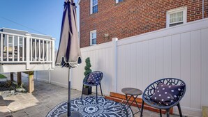 Une terrasse avec une table ronde, deux chaises et un parasol.