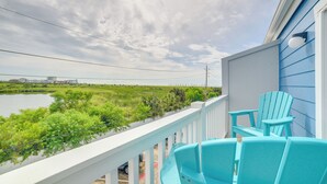 A balcony with a view of a body of water and greenery, featuring two turquoise Adirondack chairs.