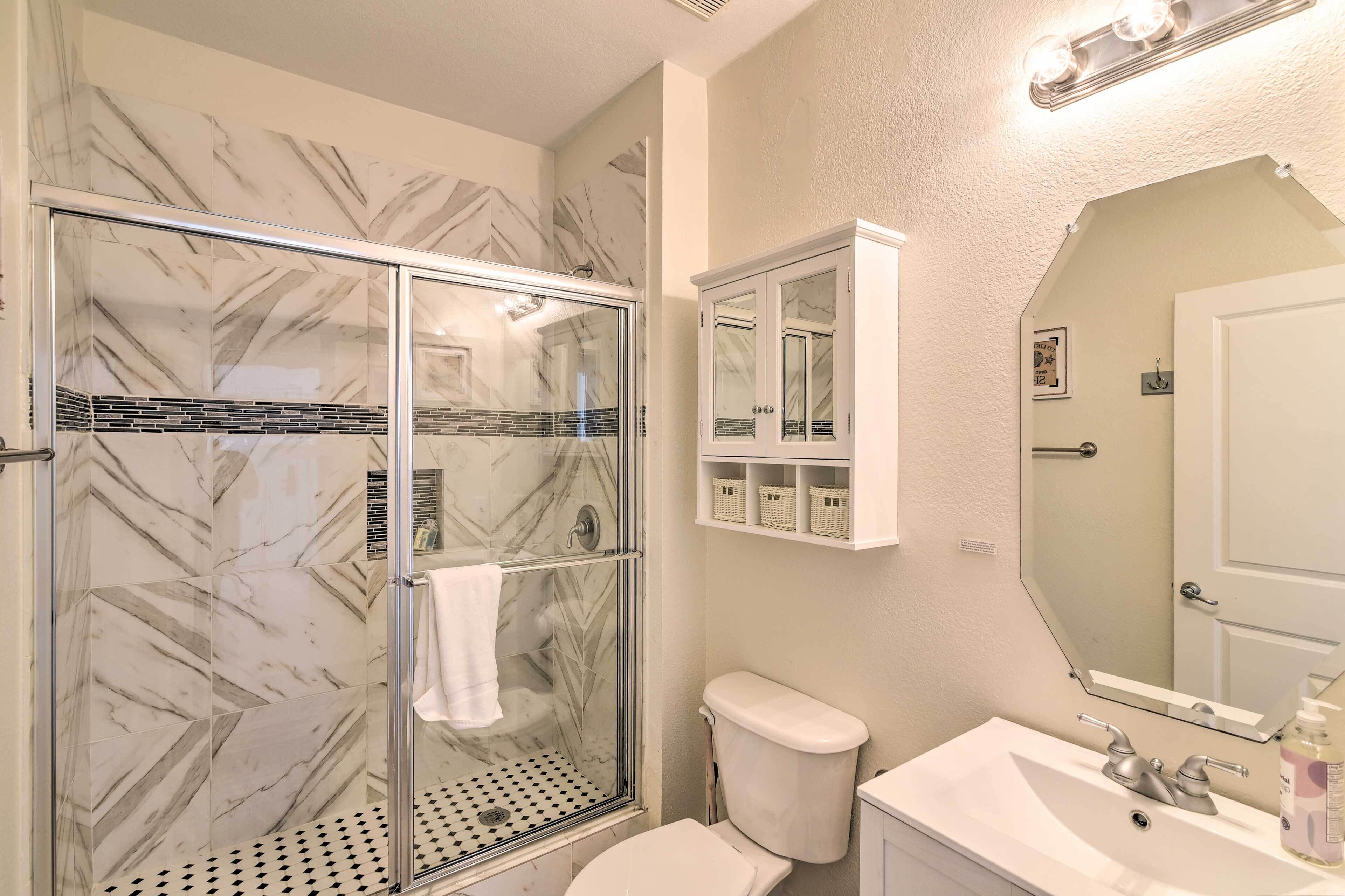 A bathroom with a glass shower enclosure, a toilet, a sink, and a mirror.