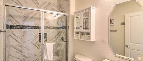 A bathroom with a glass shower enclosure, a toilet, a sink, and a mirror.
