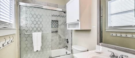 Un baño con ducha de vidrio, inodoro blanco y lavamanos con espejo.