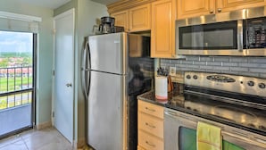 A kitchen with stainless steel appliances, wooden cabinets, and a view of a green landscape through a window. - Idyllic PCB Condo w/ Pool Access & Ocean Views! (Panama City Beach)