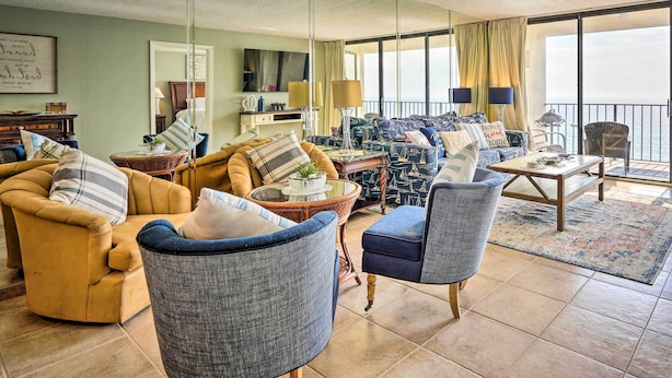 A spacious living room with a large window, a sofa set, a coffee table, and a TV. - Idyllic PCB Condo w/ Pool Access & Ocean Views! (Panama City Beach)