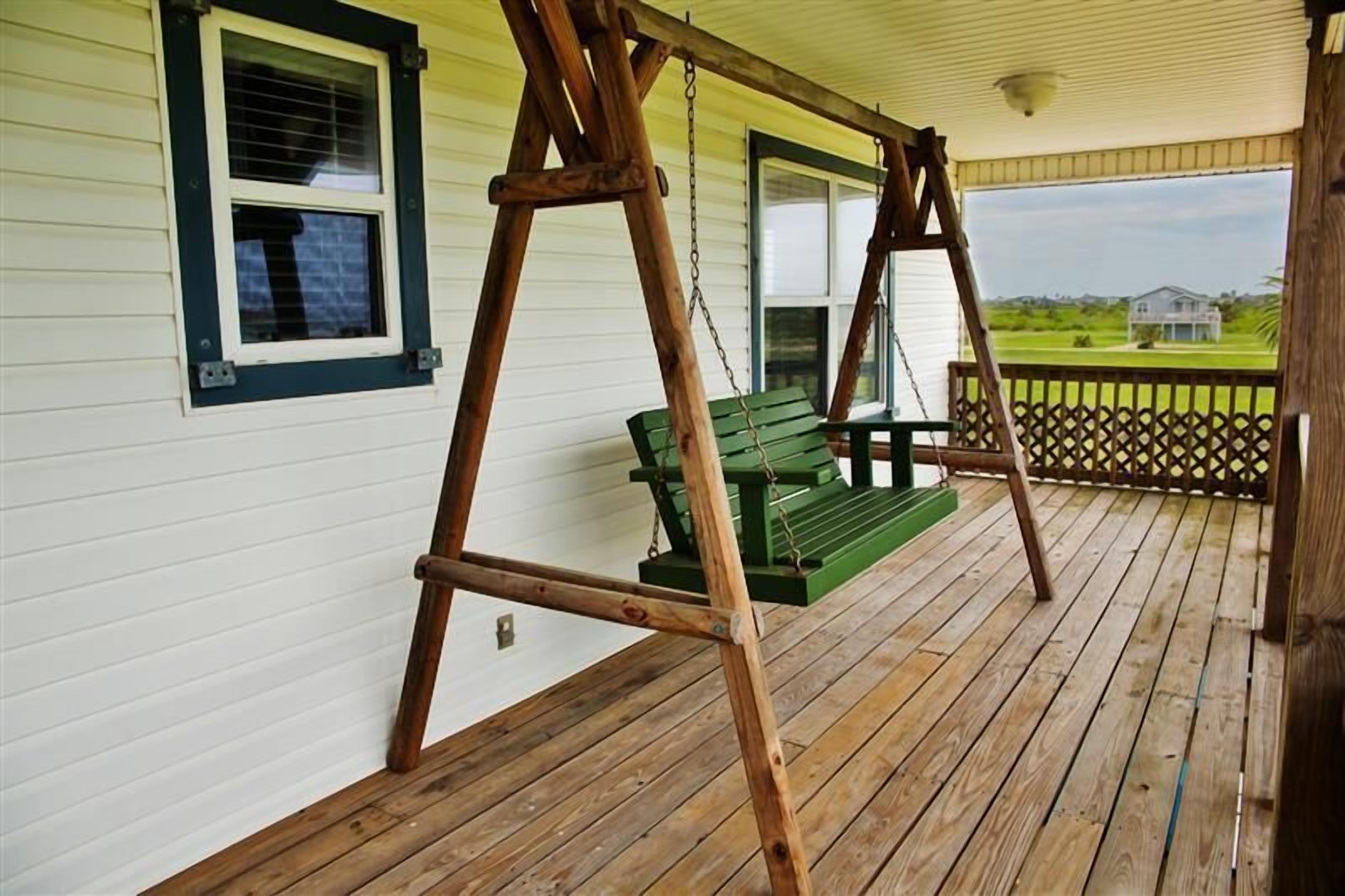 A wooden porch with a swing set and a green bench.