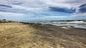 A beach with a wooden fence, a sandy shore, and a clear sky. - 1/2 Mi to Beach: Canal-front Galveston Home! (Galveston)