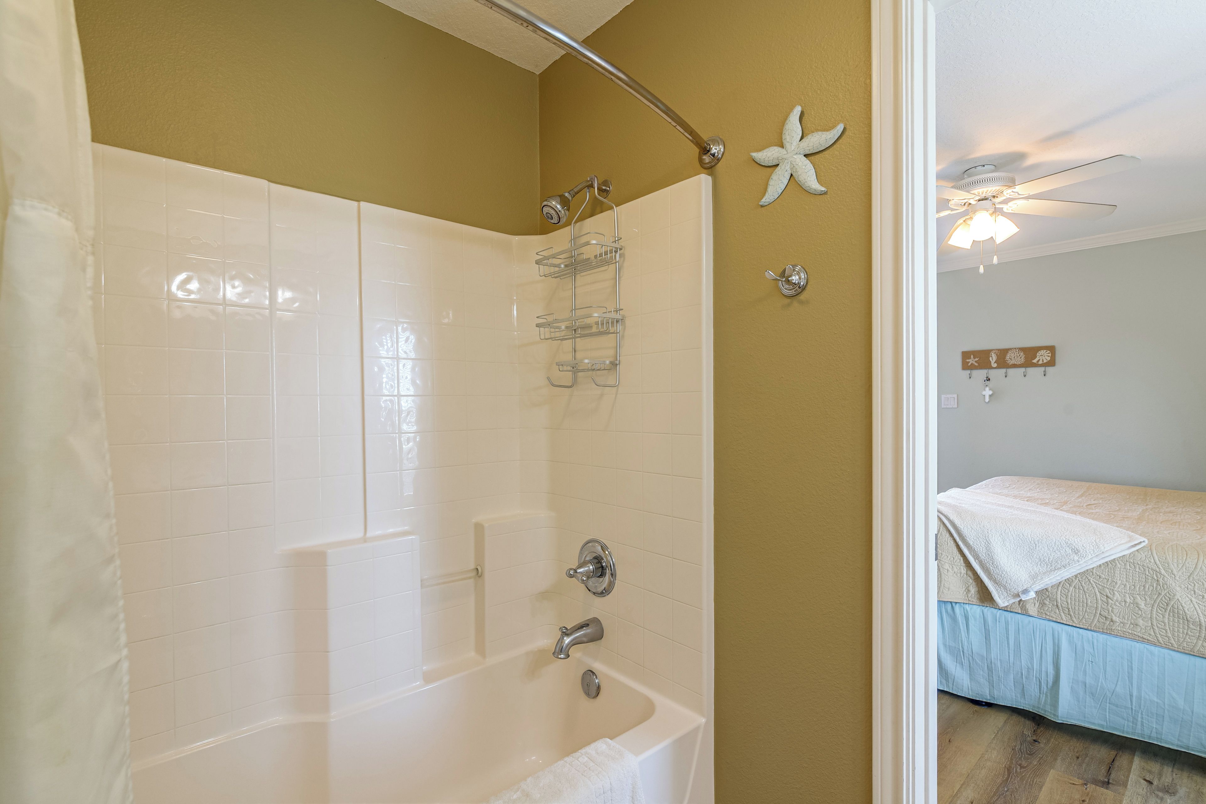 Un baño con bañera, ducha e inodoro. Hay un perchero y una decoración de estrella de mar en la pared.