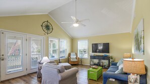 A spacious living room with a ceiling fan, a television, and a large window with blinds. - Walk to Galveston Beach: Coastal Escape w/ Yard (Galveston)