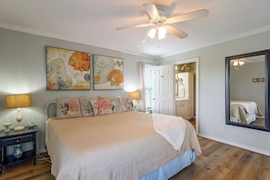 A bedroom with a bed, a ceiling fan, artwork on the wall, and a mirror.