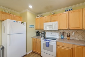 A kitchen with wooden cabinets, a white refrigerator, a microwave, a stove, and various kitchen appliances. - Walk to Galveston Beach: Coastal Escape w/ Yard (Galveston)