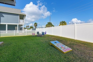 A backyard with a grassy lawn, a white fence, and a house with a balcony. - Walk to Galveston Beach: Coastal Escape w/ Yard (Galveston)