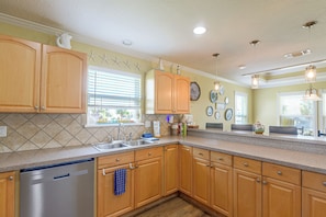 A kitchen with wooden cabinets, a dishwasher, and a window with blinds.