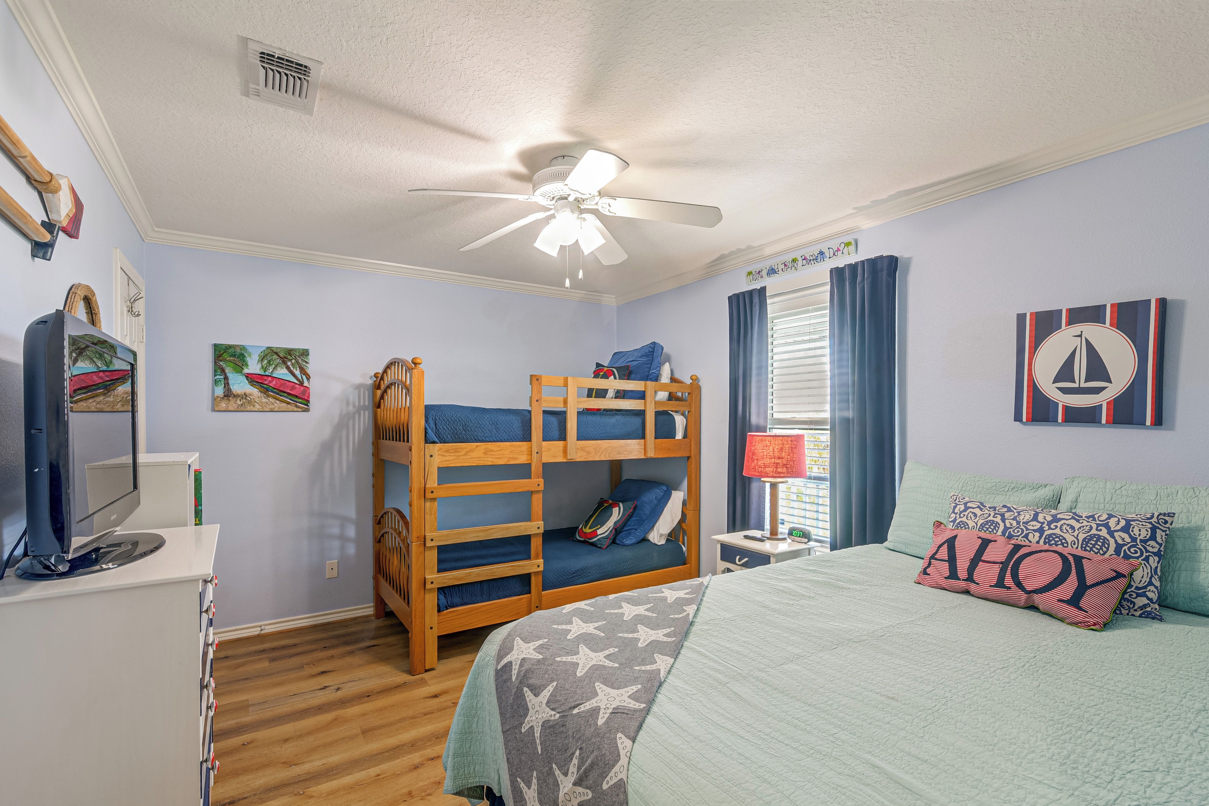 A bedroom with bunk beds, a desk, a computer, a ceiling fan, and nautical-themed decorations.
