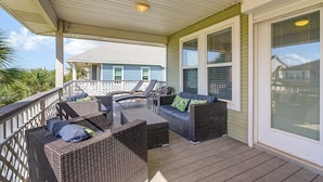 A covered porch with wicker furniture and a view of a house. - Walk to Galveston Beach: Coastal Escape w/ Yard (Galveston)