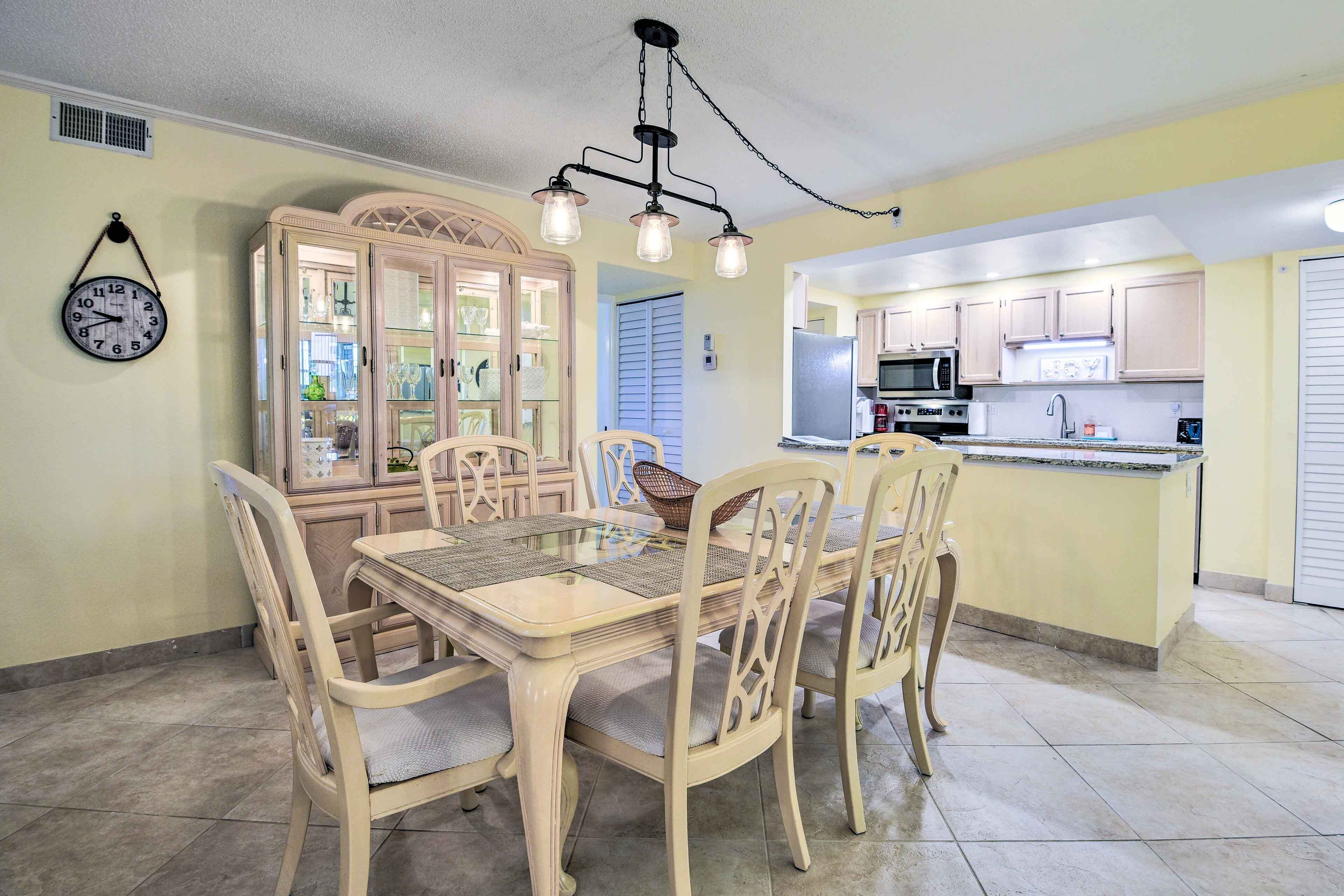 A dining area with a wooden table and chairs, a chandelier, and a clock on the wall.
