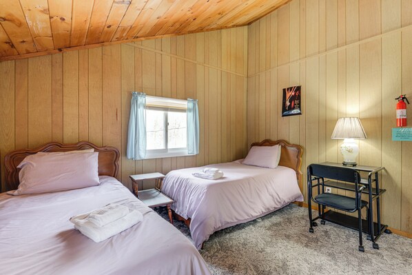 A room with two beds, a desk, a chair, a lamp, and a fire extinguisher.