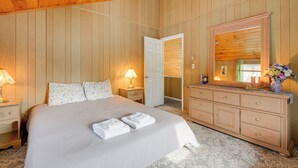 A bedroom with a large bed, wooden walls, a dresser, and a mirror. - Near Hiking & Skiing: Home in Wilmington! (Wilmington)