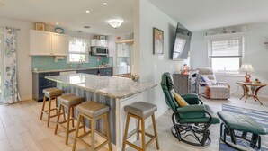 A modern kitchen with a central island, bar stools, a green rocking chair, and a view of the living area. - Families w/ Pets! Home 4 Mi to Ocean City Beach (Berlin)