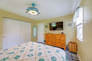 Een slaapkamer met een bed, een dressoir, een televisie en een plafondventilator.
