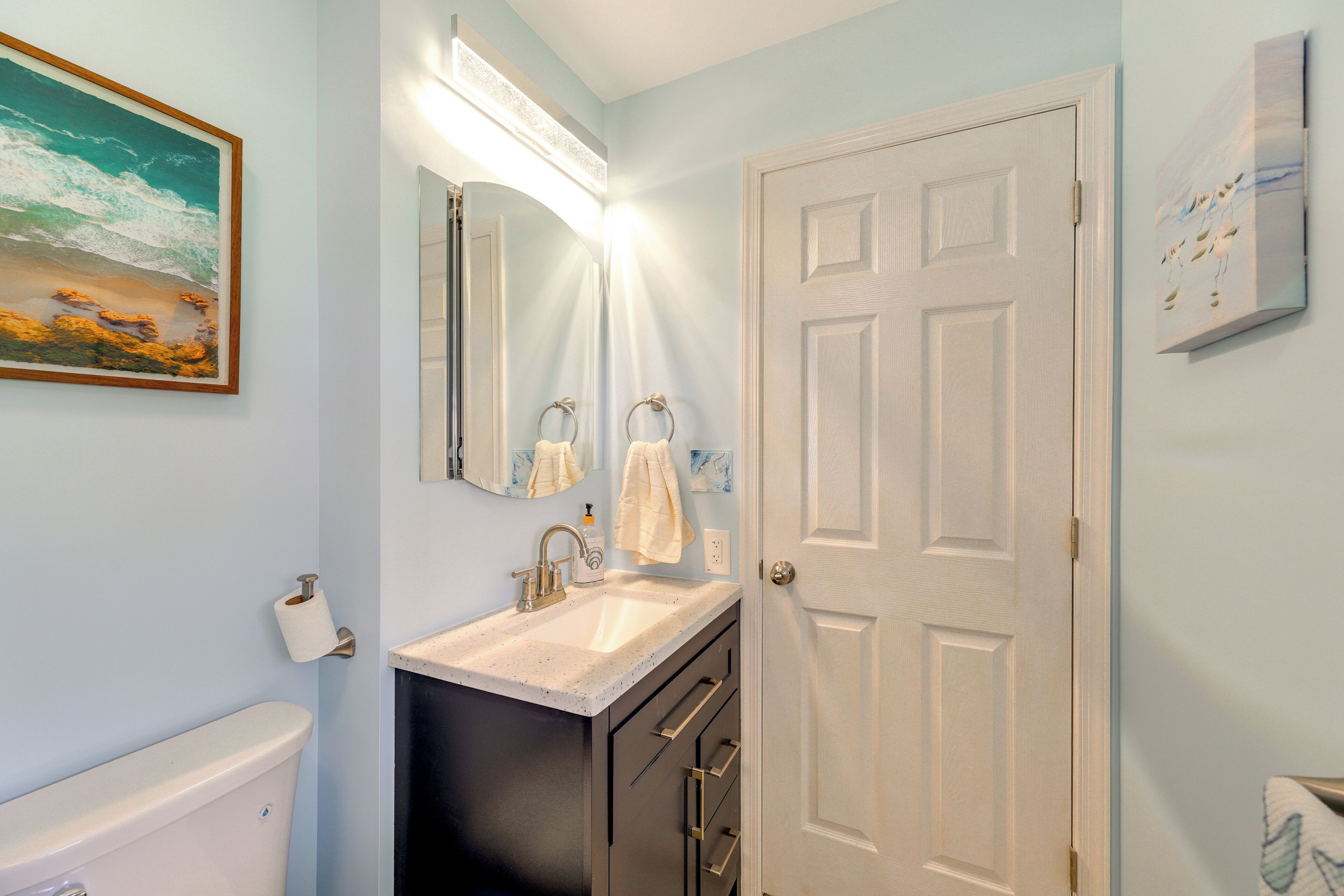 A bathroom with a toilet, sink, mirror, and towel rack.