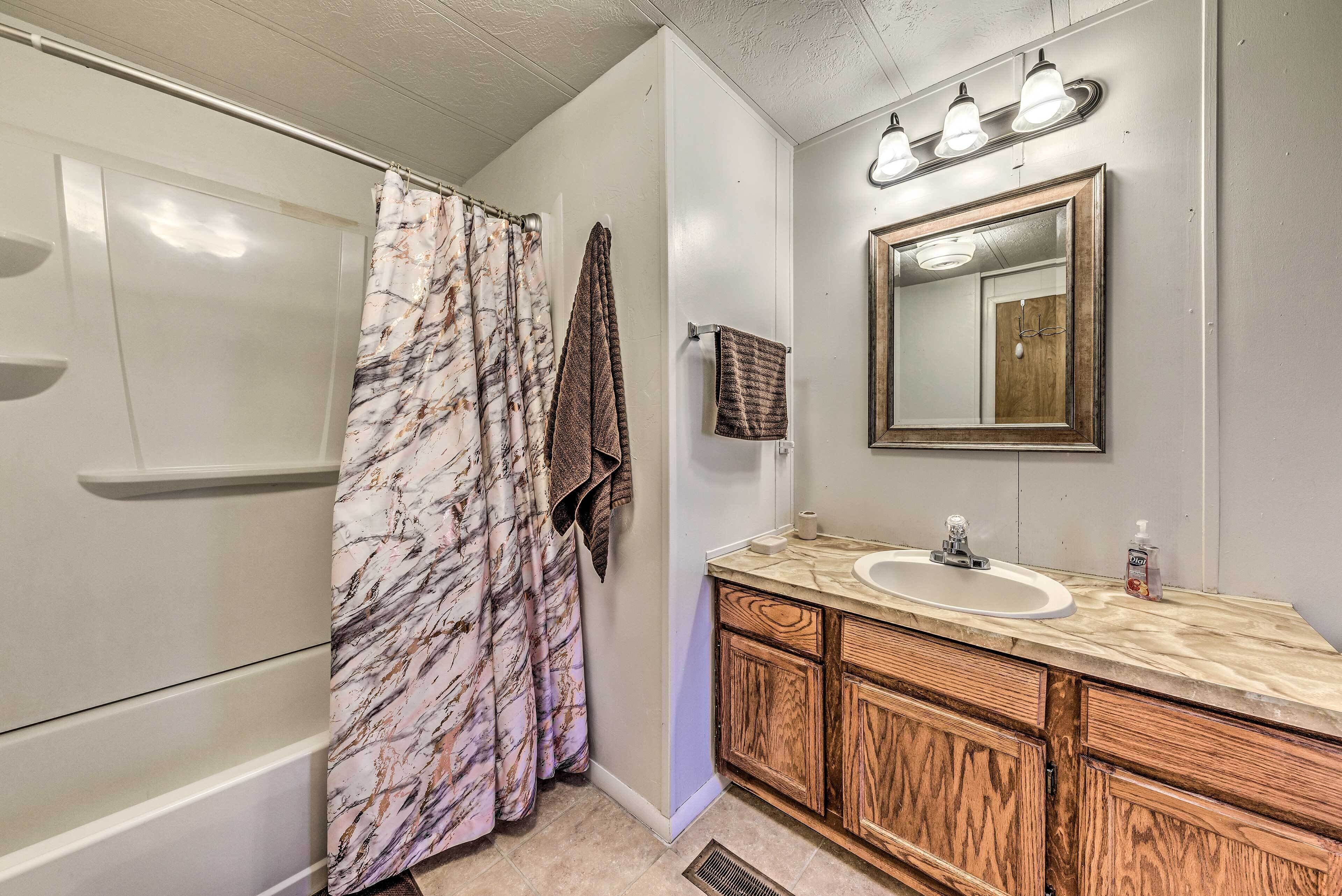 A bathroom with a shower, a sink with a wooden vanity, a mirror with lights, and a marble-patterned shower curtain.