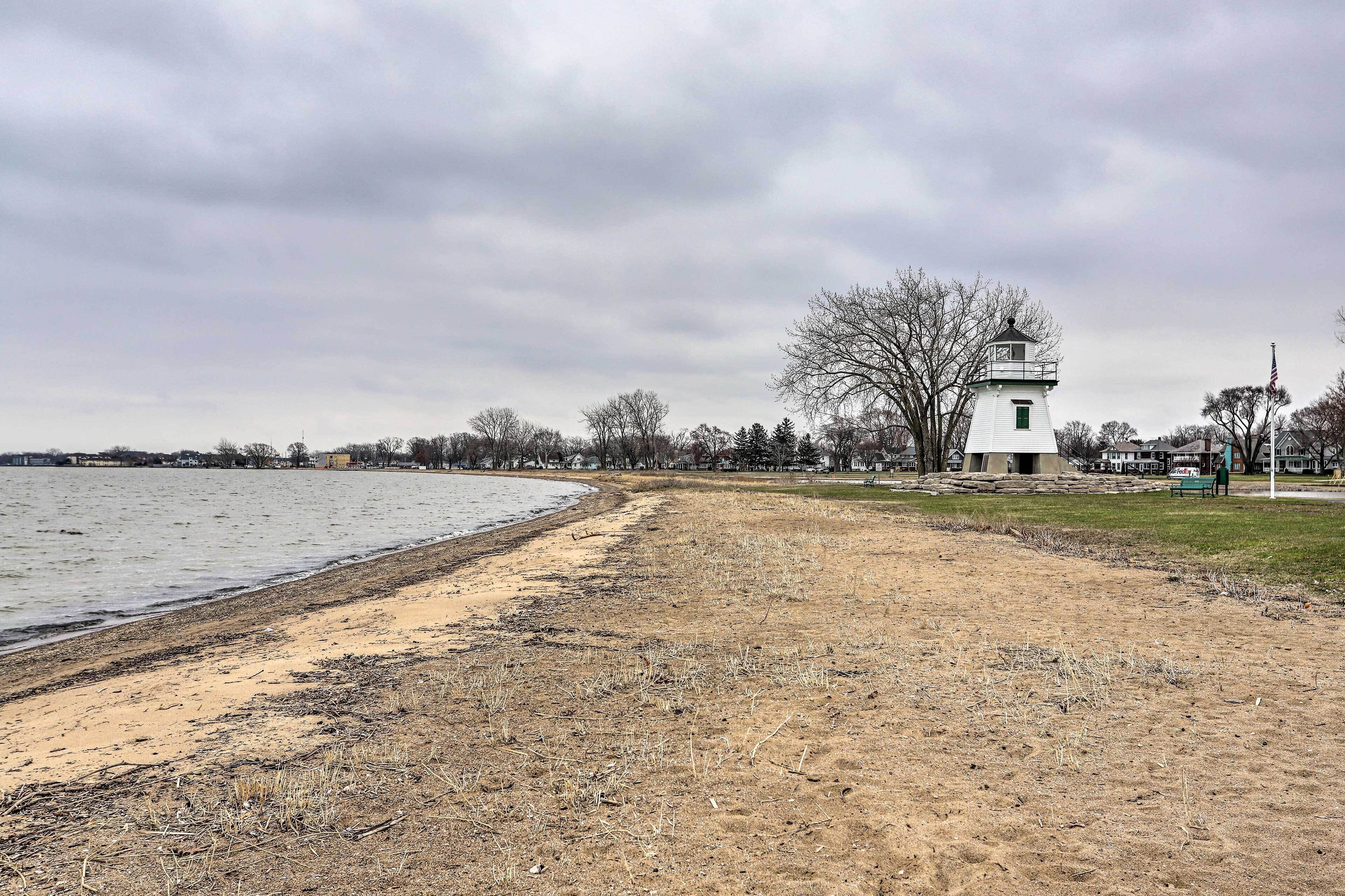 A lighthouse by a beach with a grassy area and trees in the background.