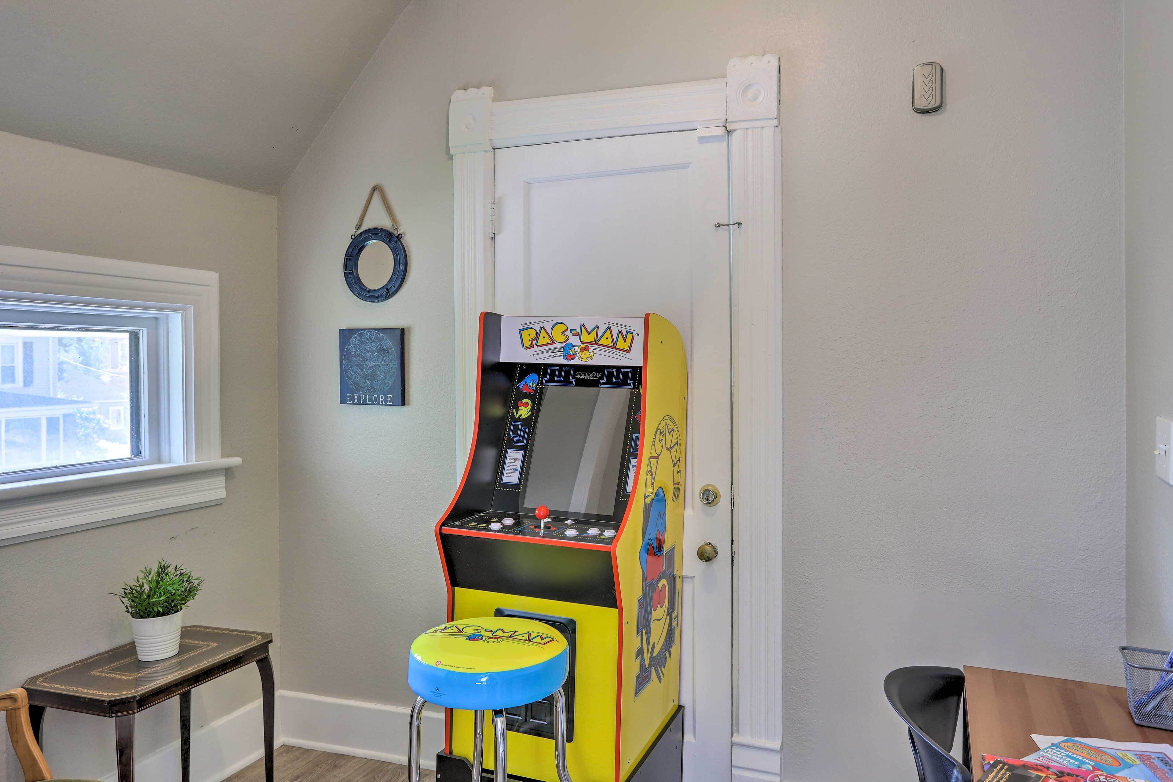 Une pièce avec une borne d’arcade Pac-Man, une petite table avec une plante et une fenêtre.