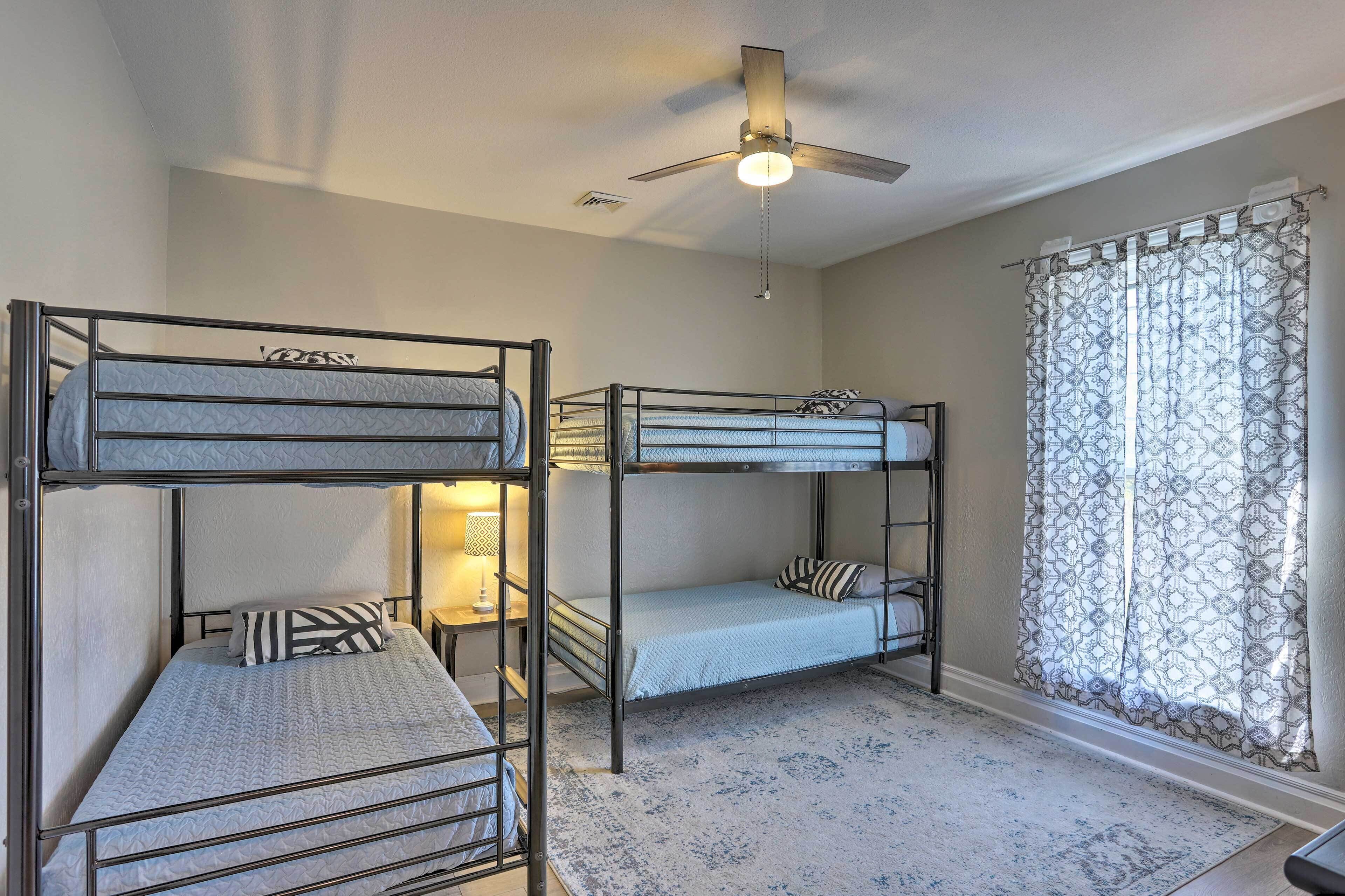 A room with bunk beds, a ceiling fan, and a patterned curtain.