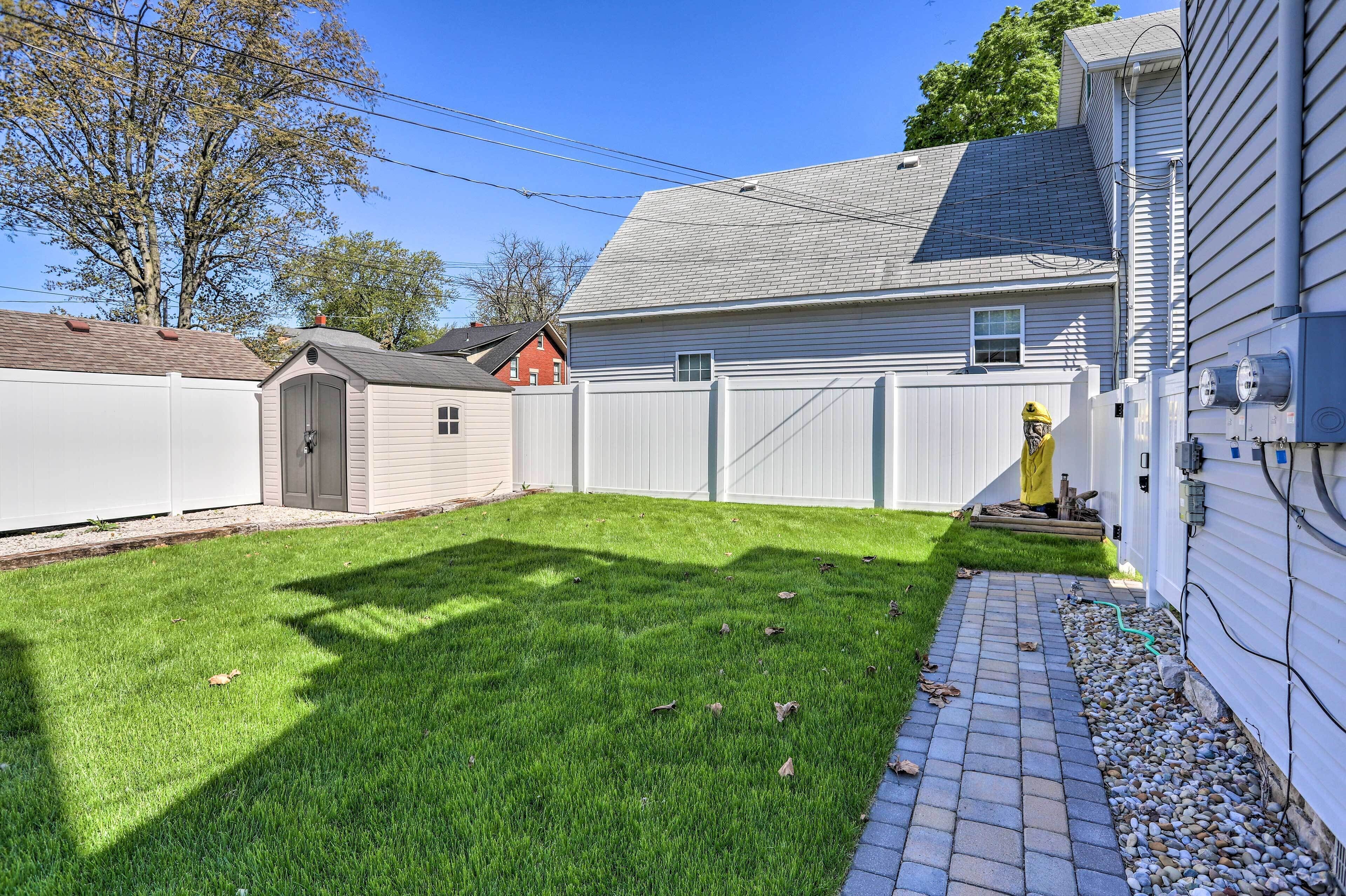 A backyard with a paved pathway, a small shed, and a house with a white exterior.