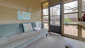 A room with a light blue sofa, a world map on the wall, and a view of the backyard through a large window. - 6 Mi to Dtwn Austin: Home w/ Screened Porch & Yard (Austin)