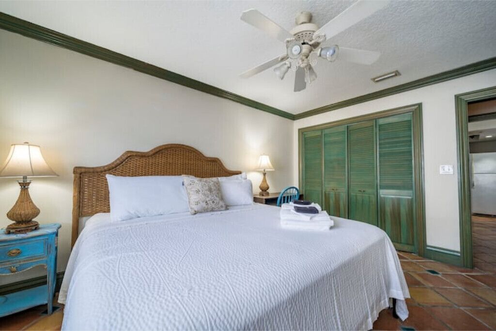 Quarto com cama, duas luminárias de cabeceira, ventoinha no teto e portas verdes.