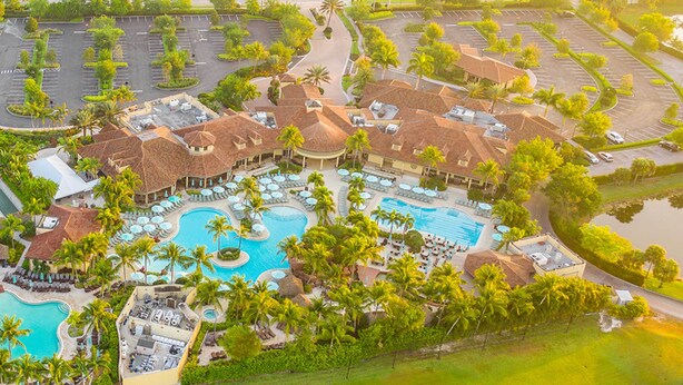 Luchtbeeld van een resort met meerdere zwembaden, palmbomen en een parkeerplaats.