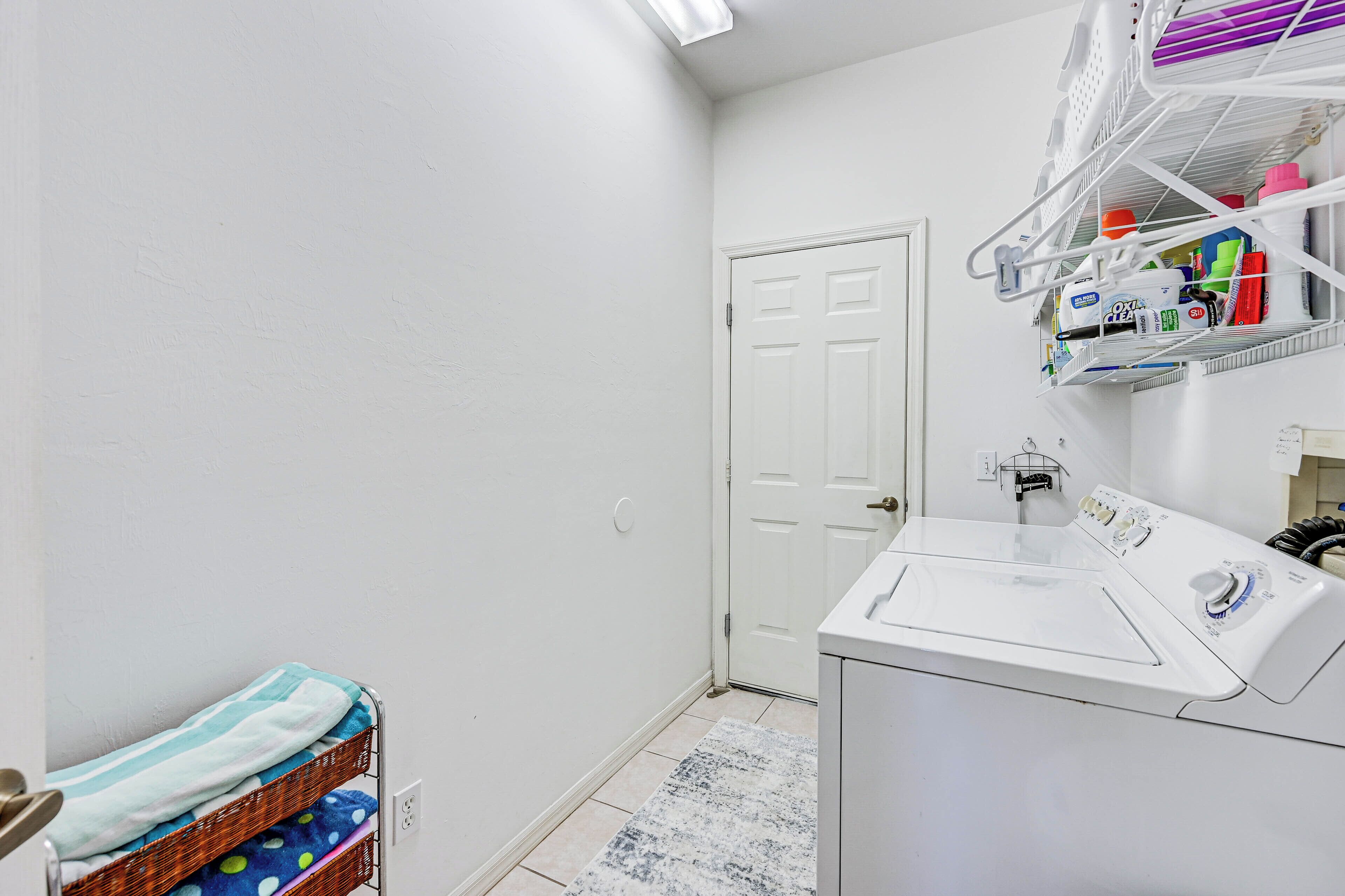 A laundry room with a white washing machine, a drying rack, and a basket of folded clothes.